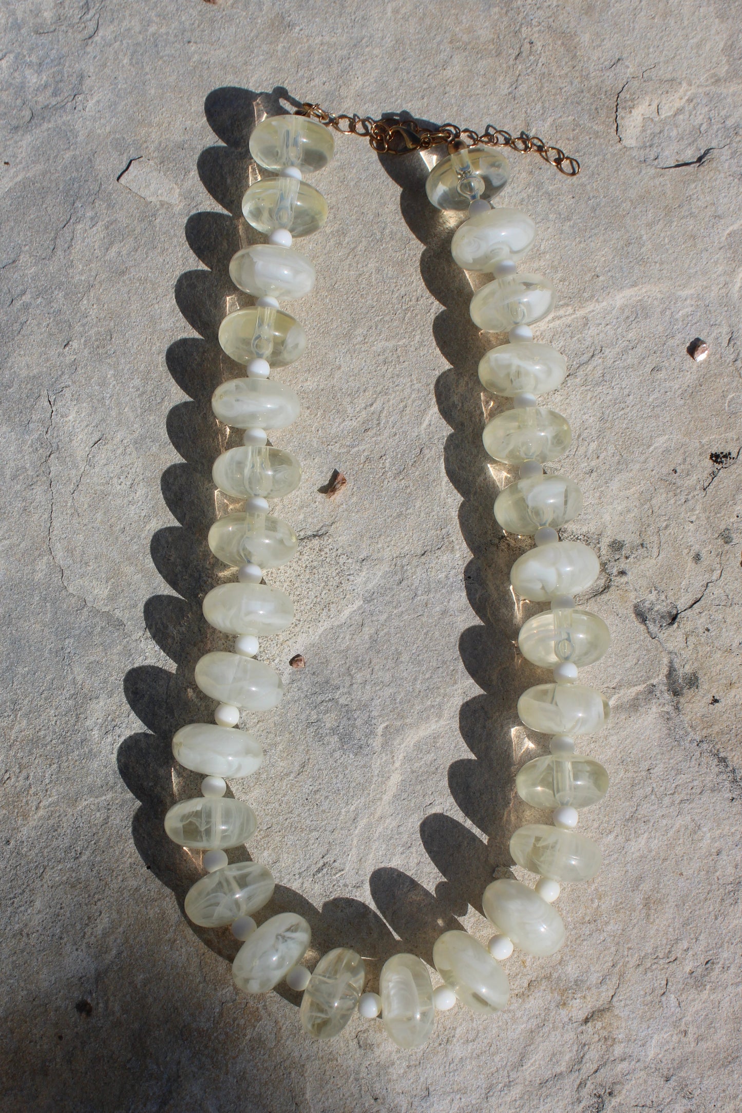 A beaded necklace made of translucent pale green gemstone beads, laid out on a textured gray stone surface.