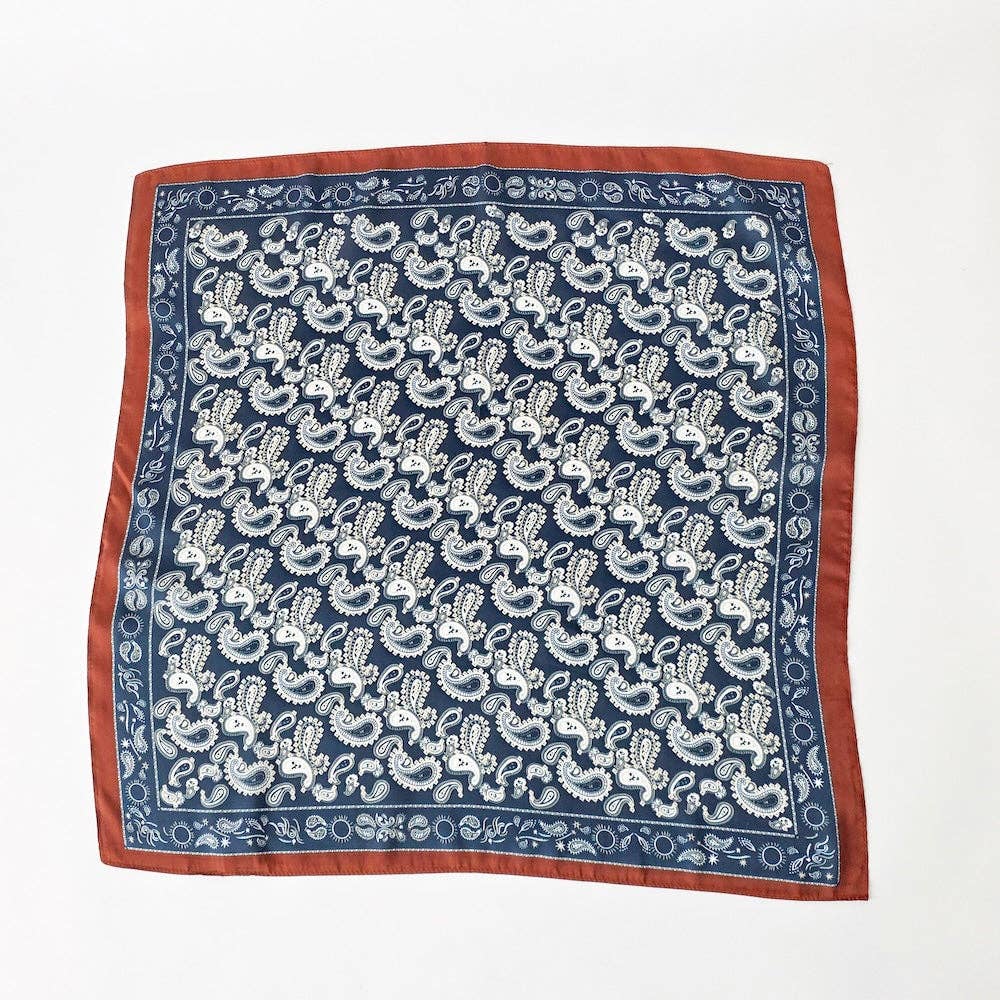 A square silk scarf featuring a navy blue background with a white block-printed floral pattern and a rust-red border, laid flat on a white background.